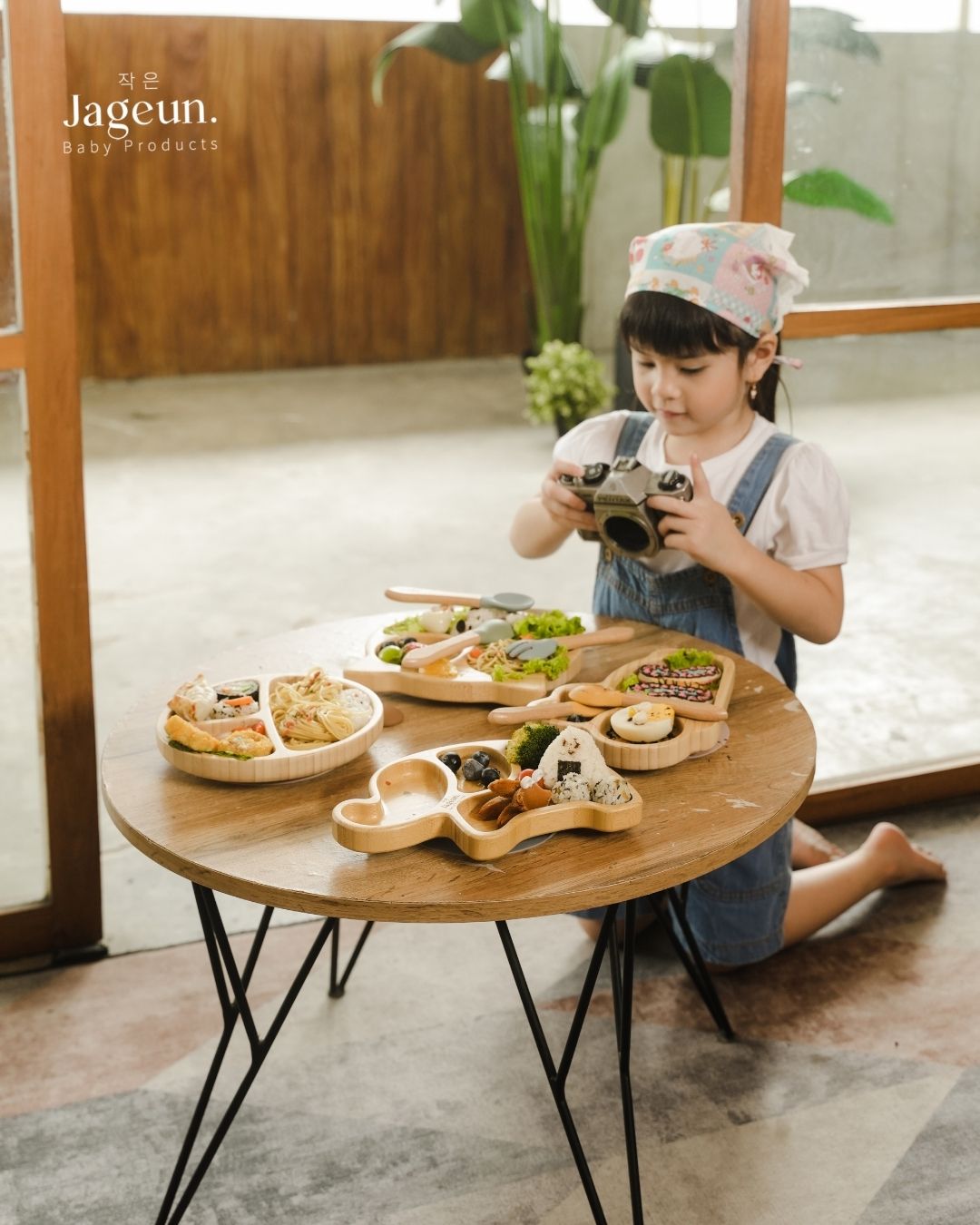 Anak kecil berlutut di dekat meja bundar dengan beberapa produk Jageun